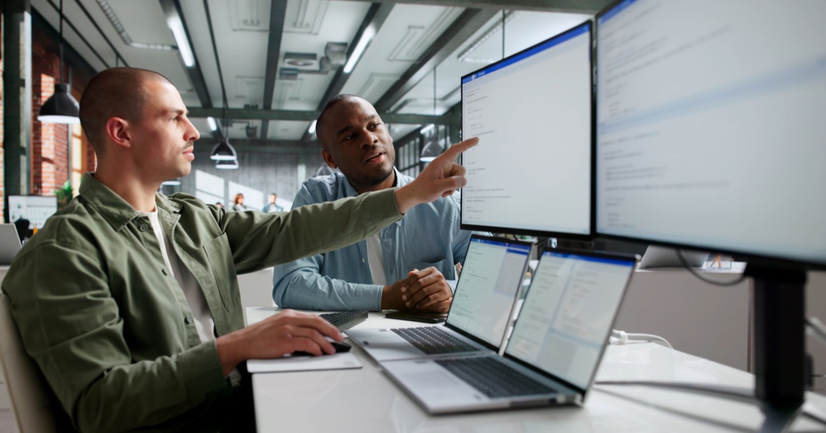 Software engineers comparing system data across multiple monitors