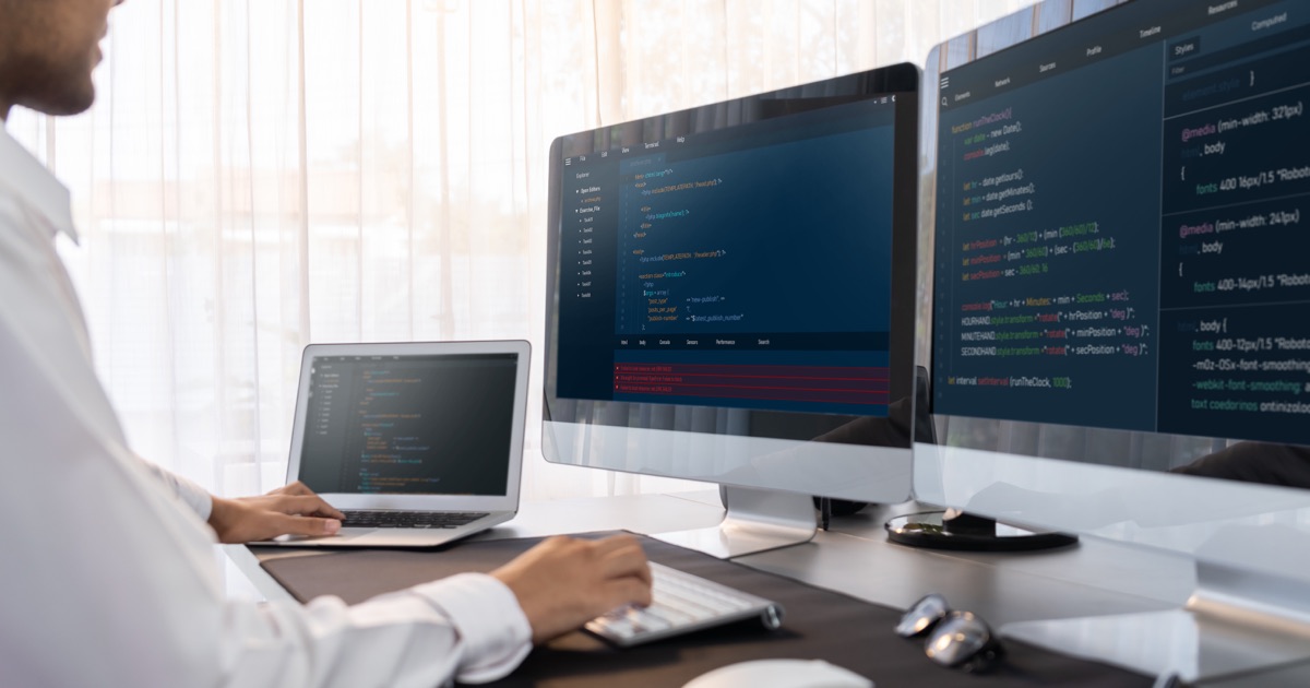 Software engineer maintaining website code on multiple computer screens